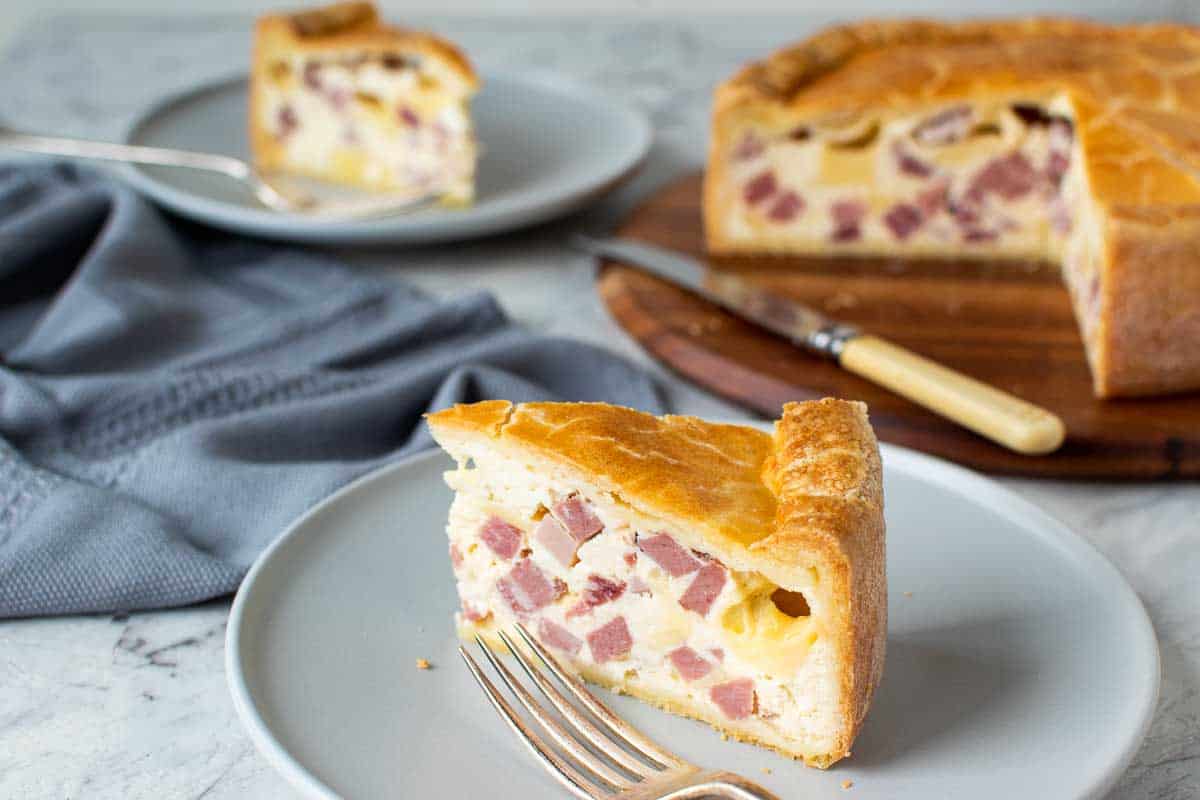 Close up of a slice of easter pie with another slice and the whole pie in the background.