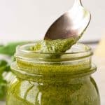Image with text. Text reads "How to make nut free pesto". Image is glass jar of pesto with a spoonful being spooned out, fresh basil in the background