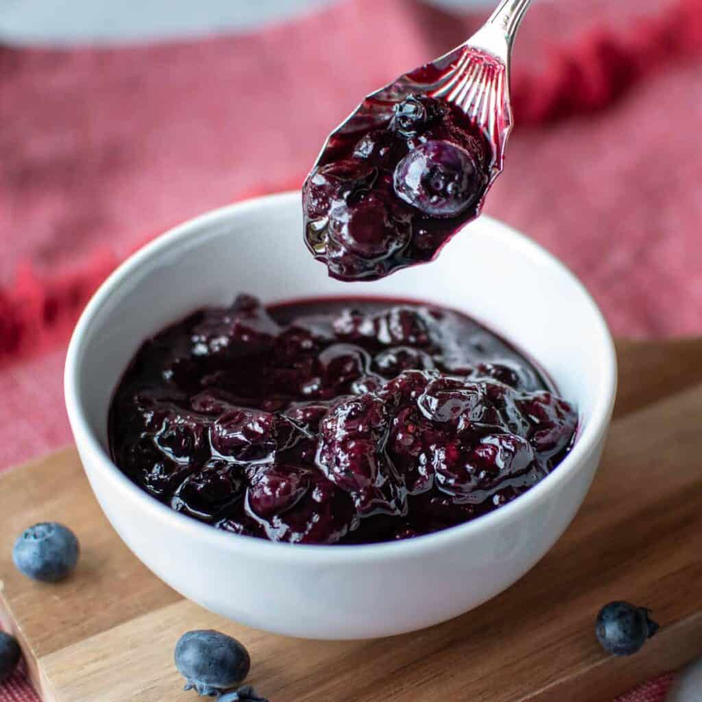 Blueberry compote in a white bowl with a spoonful lifted out.