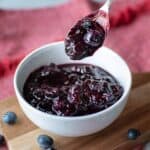 Blueberry compote in a white bowl with a spoonful lifted out.