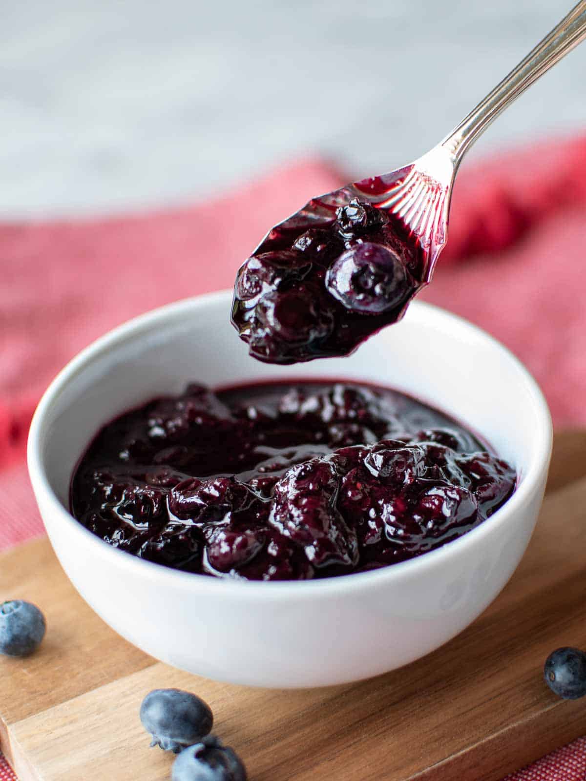The finished blueberry compote recipe in a white bowl with a spoonful lifted out.