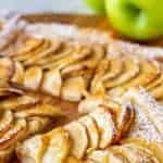 image with text. text reads 'puff pastry apple tart easy. image is slices of puff pastry apple tart on wooden board, green apple in the background.