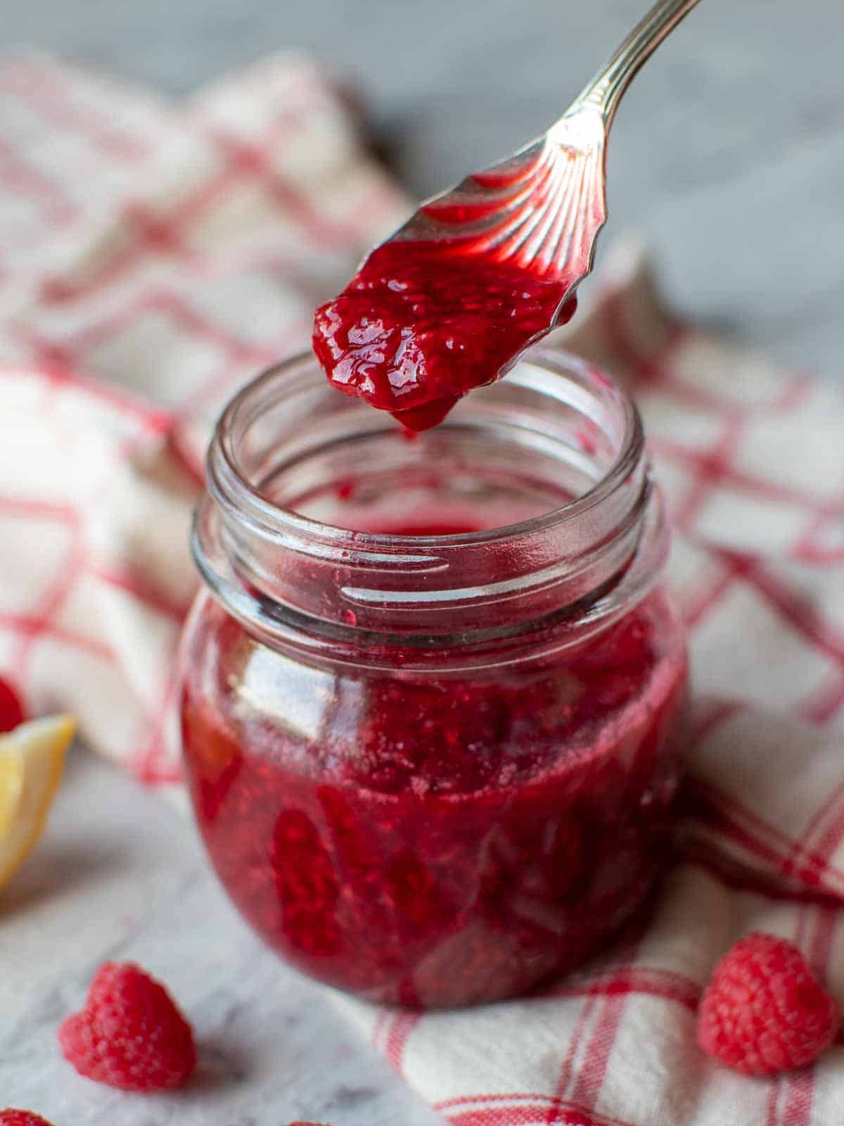 Raspberry Compote in a glass jar with a spoon full being lifted out.