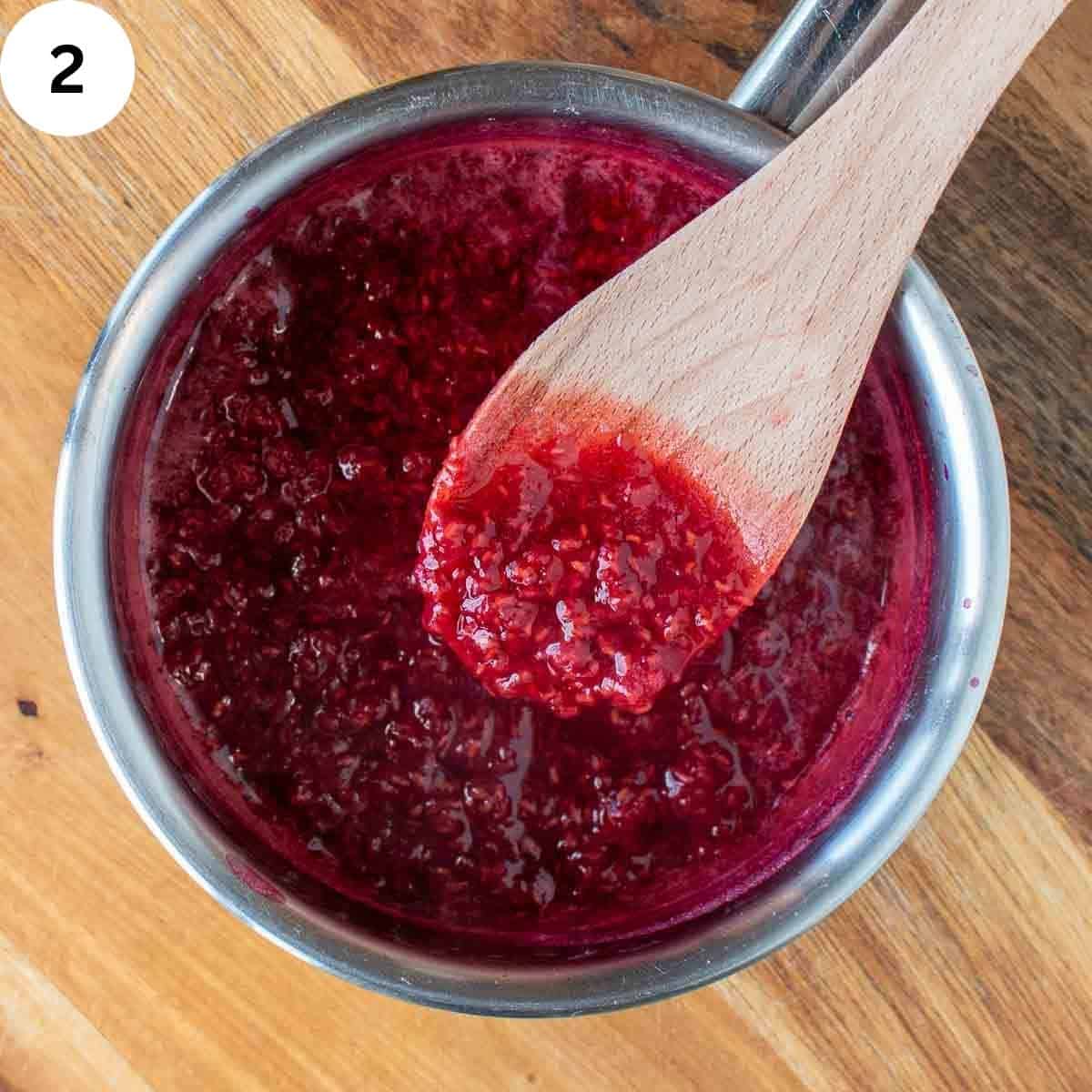 Raspberry sauce in a saucepan being stirred with a wooden spoon.