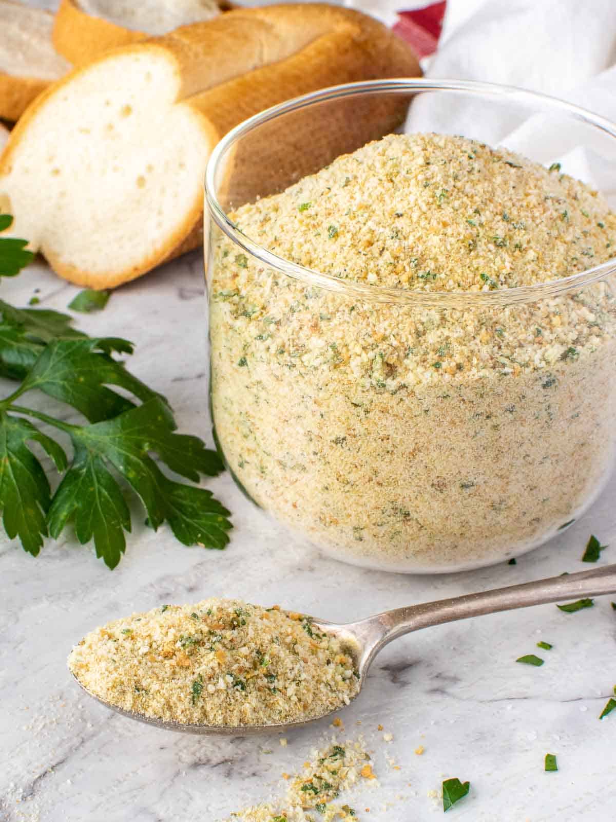 Italian bread crumbs in glass jar with a spoonful of crumbs.