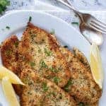 image with text. text reads crispy and tasty italian chicken cutlets. images is browned chicken cutlets on white plate with lemon wedges.