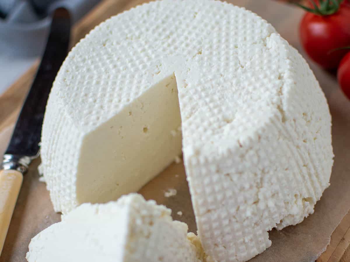 An upturned whole fresh ricotta cheese on wooden board with a wedge cut out.