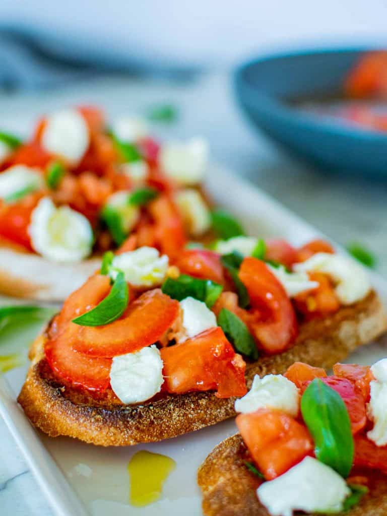 bruschetta with tomatoes and mozzarella on white plate.