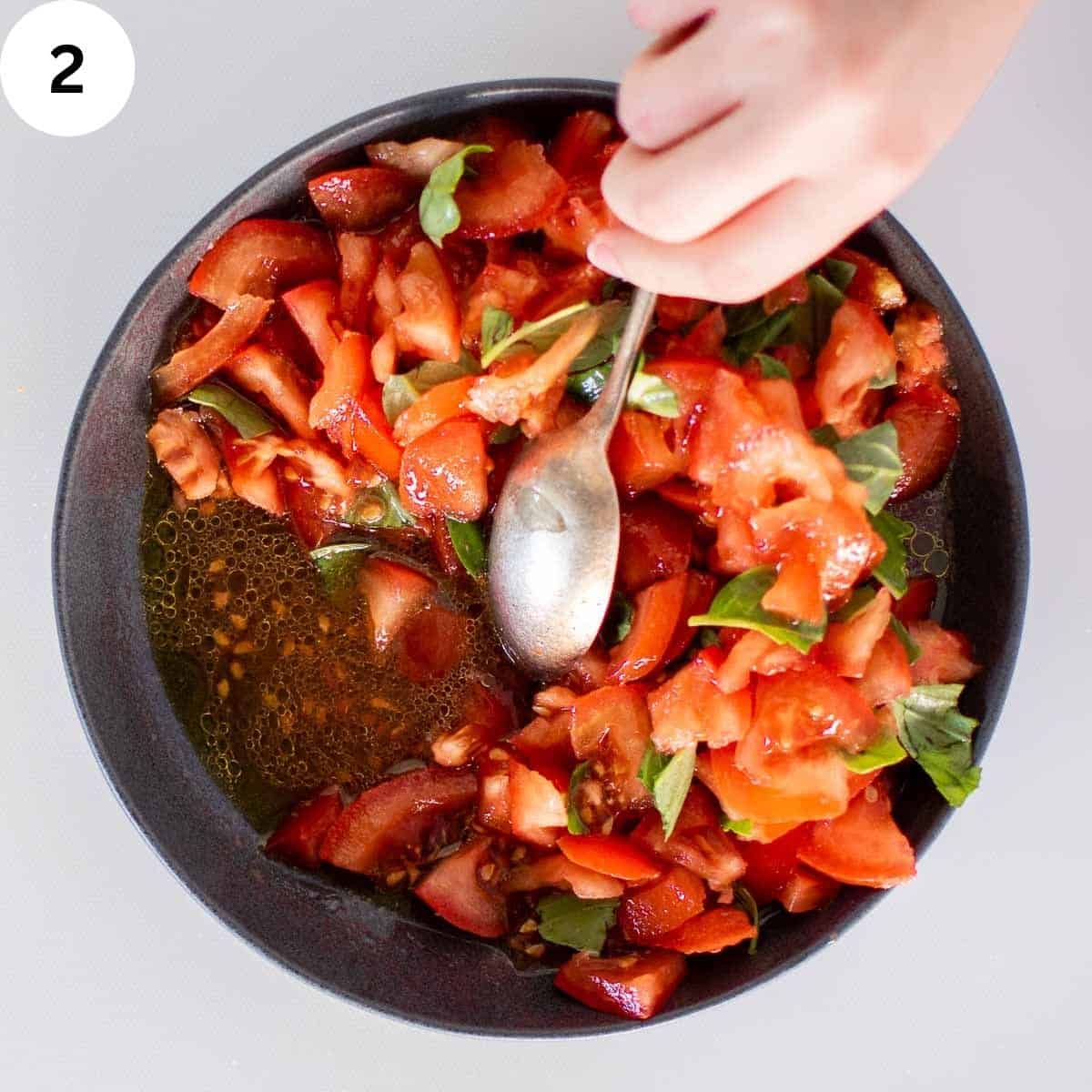 Stirring a bowl full of tomatoes with some basil.