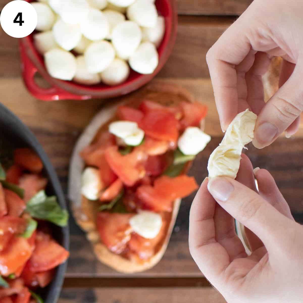 Tearing mini mozzarella balls with tomato bruschetta in the background.