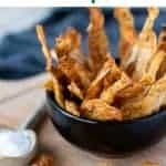image with text. text reads "crispy and delicious potato skin chips". image is potato skin chips piled into black bowl placed onto a wooden board with more chips on the board and a spoon filled with salt.