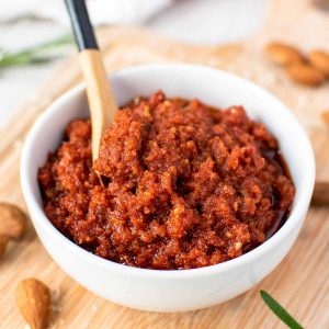 sun dried tomato pesto in a white bowl with small wooden spoon in the pesto.