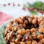 italian honey balls piled into a wreath shape on a white plate with green rosemary sprigs all around it.