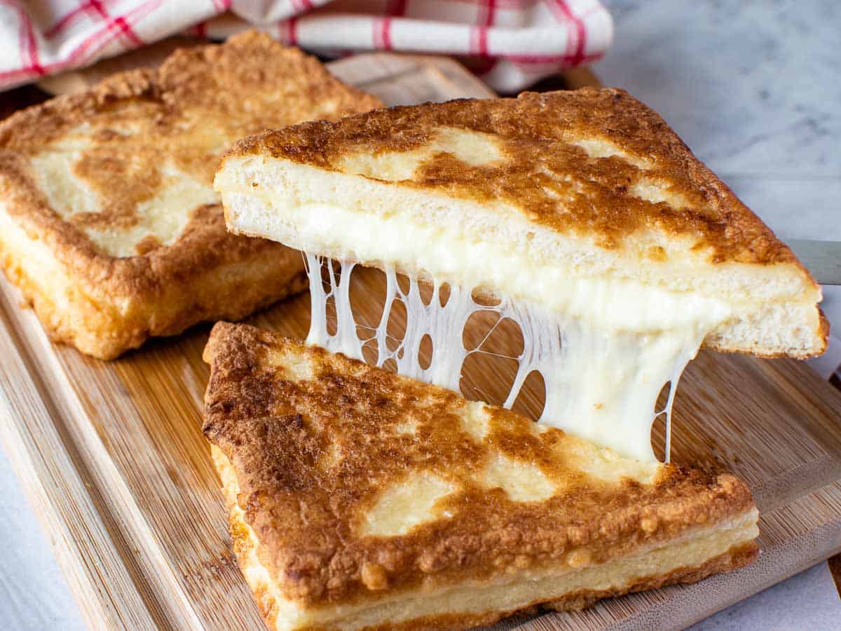 Fried sandwich cut in half and showing cheese pull with second sandwich in background.