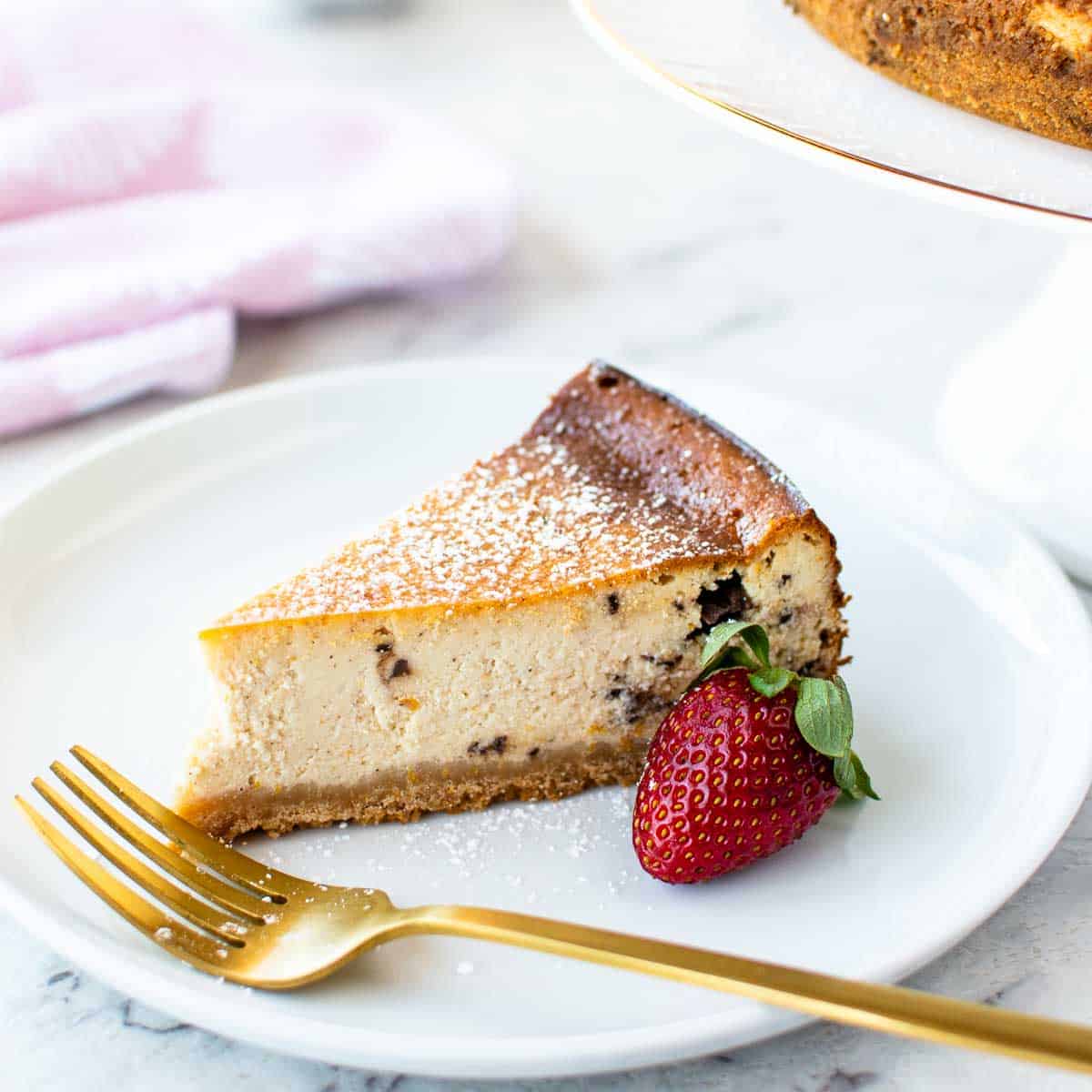A slice of ricotta cheesecake on a white plate with a strawberry on the side.