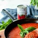 image with text. text reads 'classic Italian sauce san marzano tomato sauce'. image is tomato sauce in a black skillet with a sprig of basil in the centre.