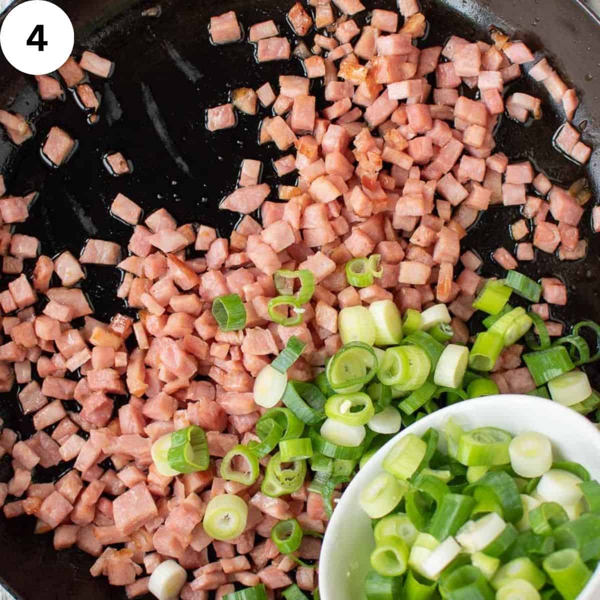 Chopped green onions being added to diced ham in a pan.