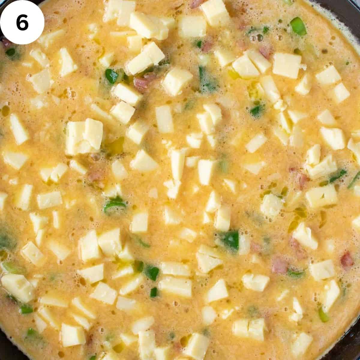 Overhead view of uncooked frittata with cubes of cheese visable.