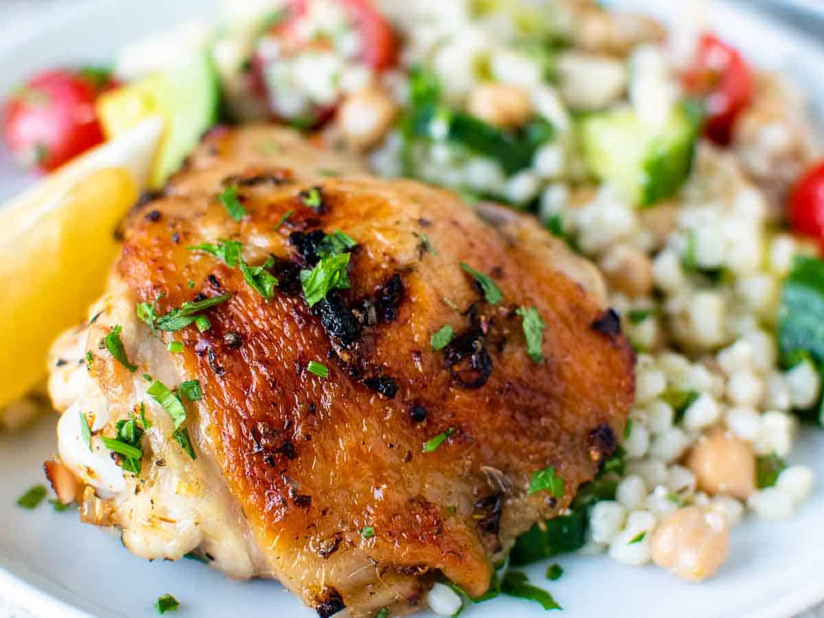 Close up of baked chicken thigh plated with side salad.