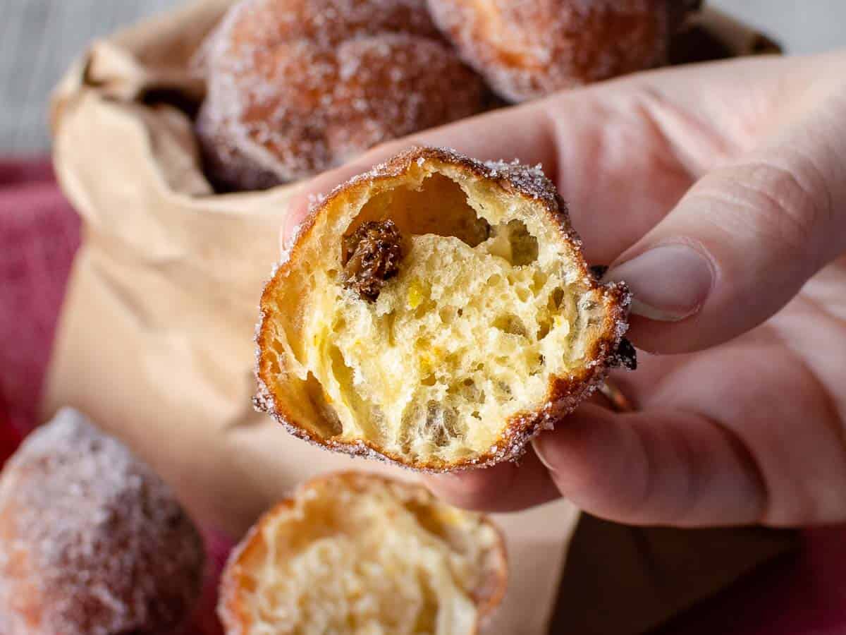 Close up of theThese Frittelle are the perfect combination of crispy on the outside and chewy on the inside. inside of a fried dough ball held by fingers.