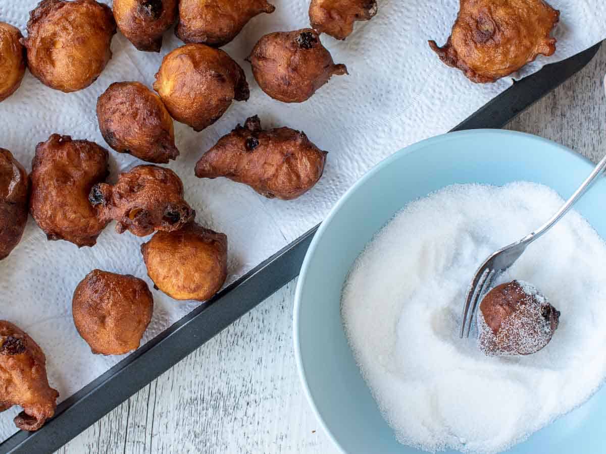 Fried dough balls being coated in granulated sugar.