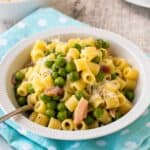 Pasta and peas in a white bowl on a sky blue napkin.
