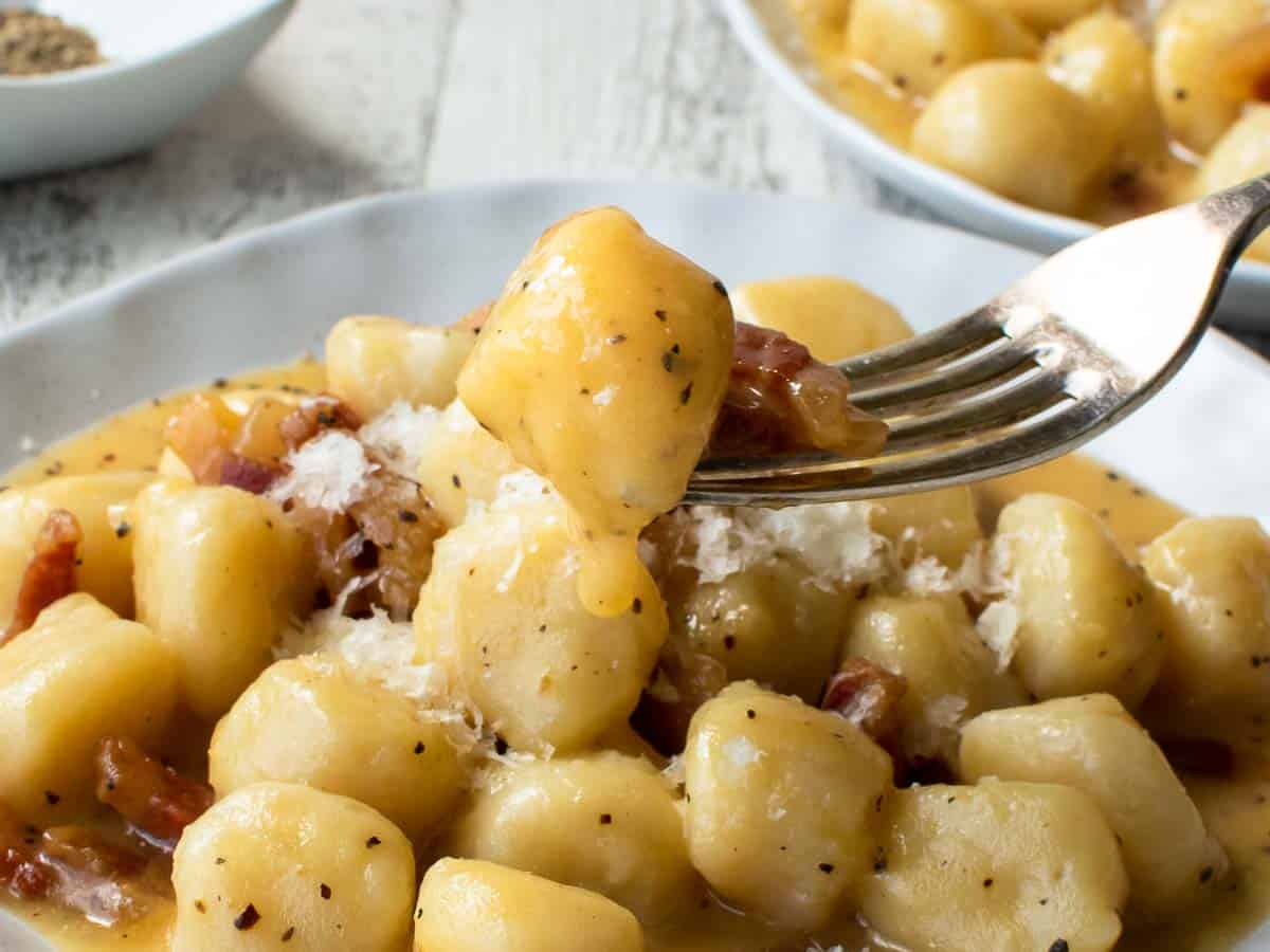 Close up of gnocchi on a fork with more in the background.