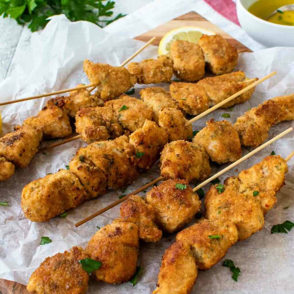 Chicken Spiedini on white baking paper with lemon wedges.