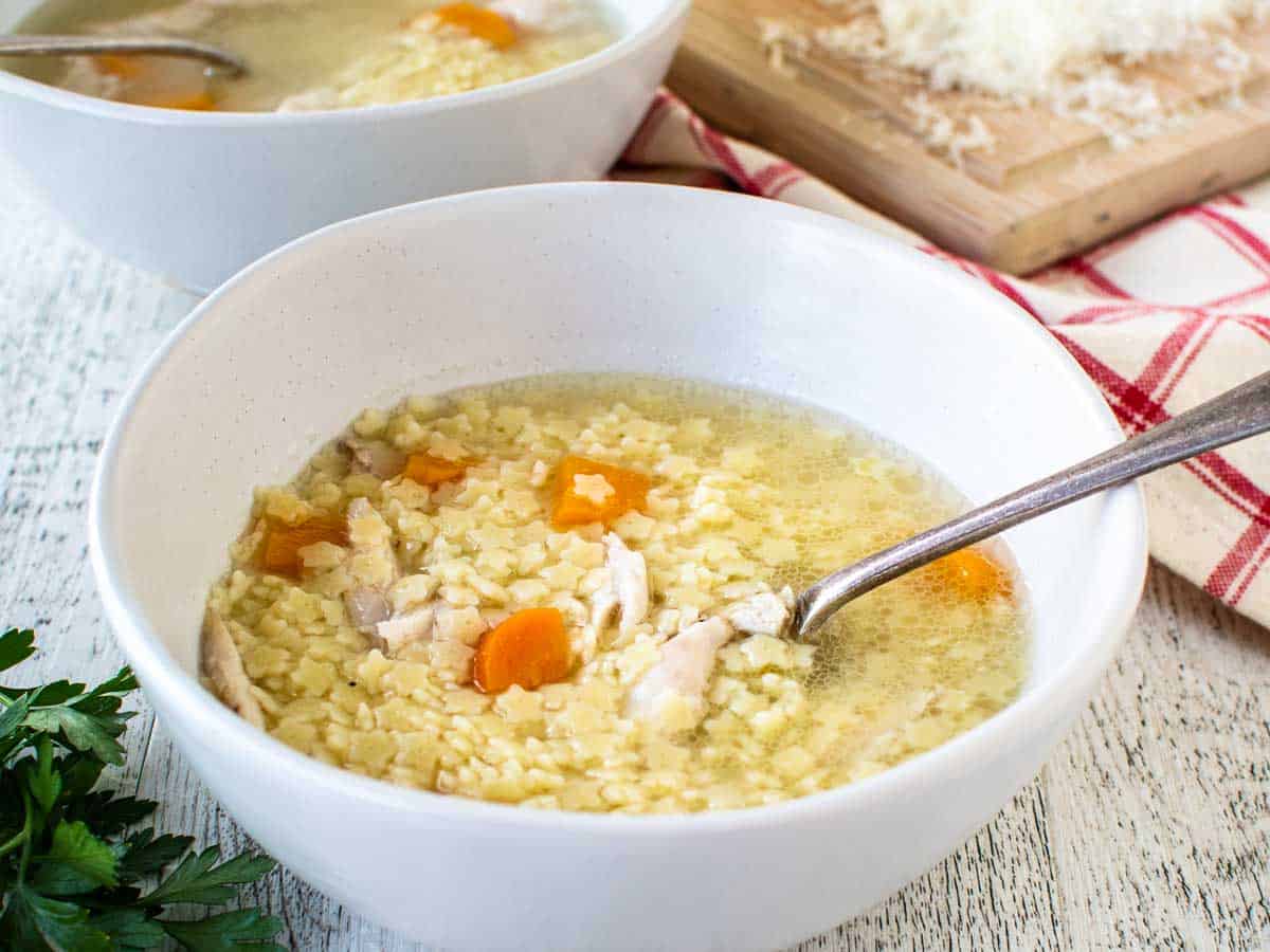 White bowl filled with pasta and chicken broth.