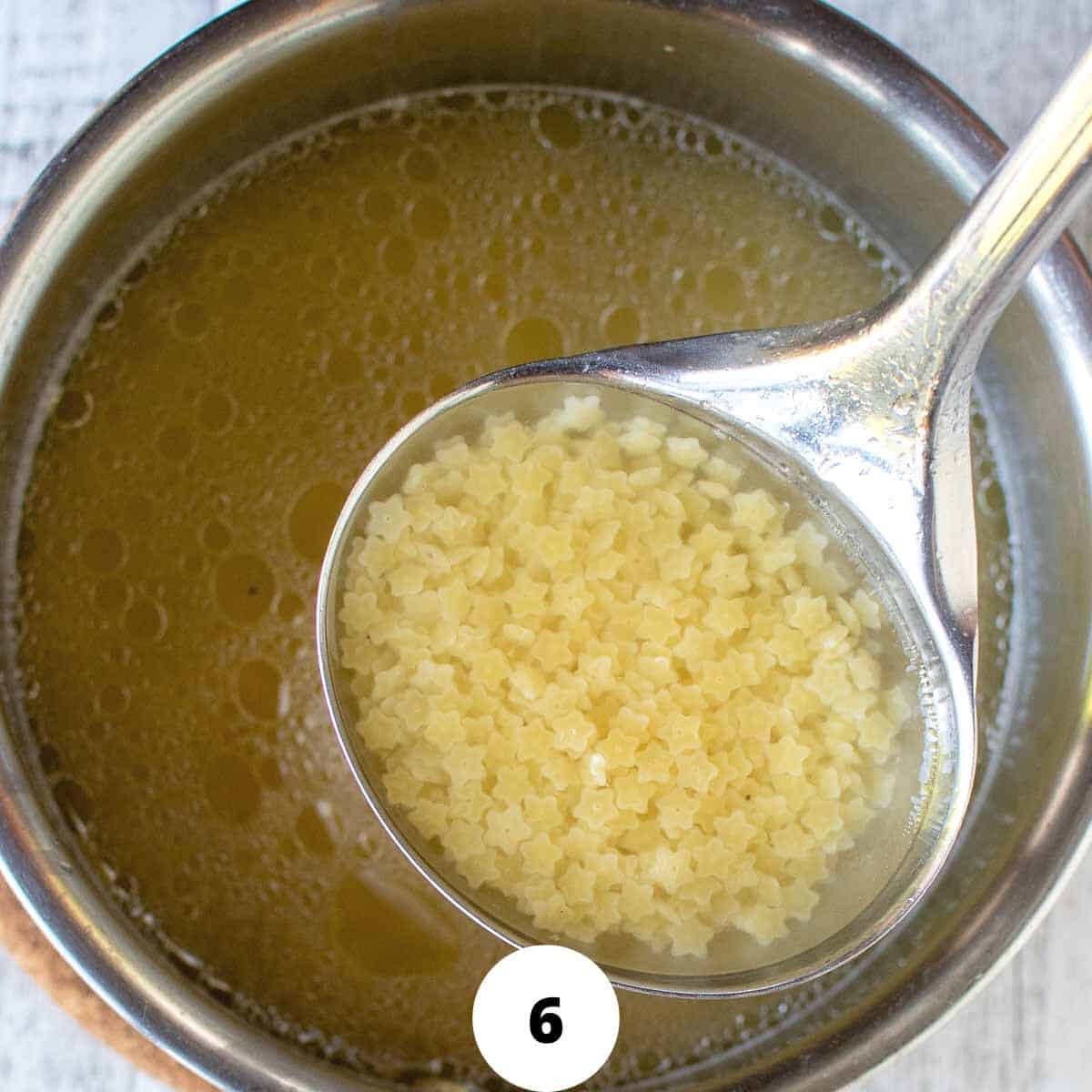 Ladling out small star pasta and broth from pot.