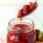 Strawberry Compote in a glass jar with a spoonful being poured in.