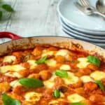 Gnocchi alla sorrentina in a round red pan with plate in the background.