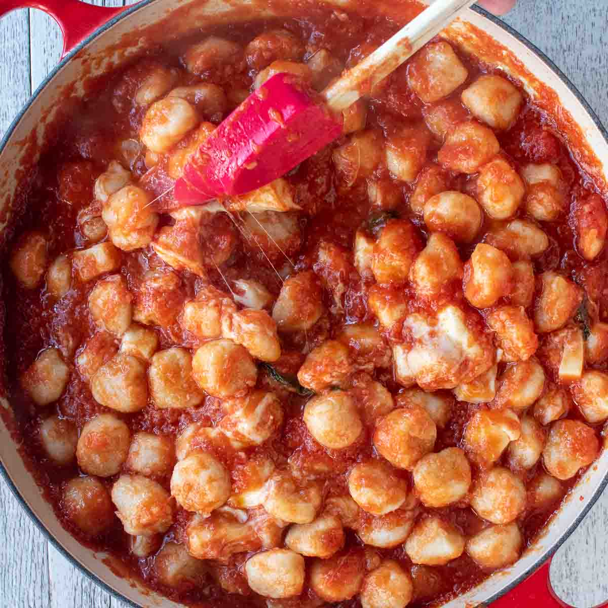 Overhead view of gnocchi in tomato sauce and cheese pulling strings.