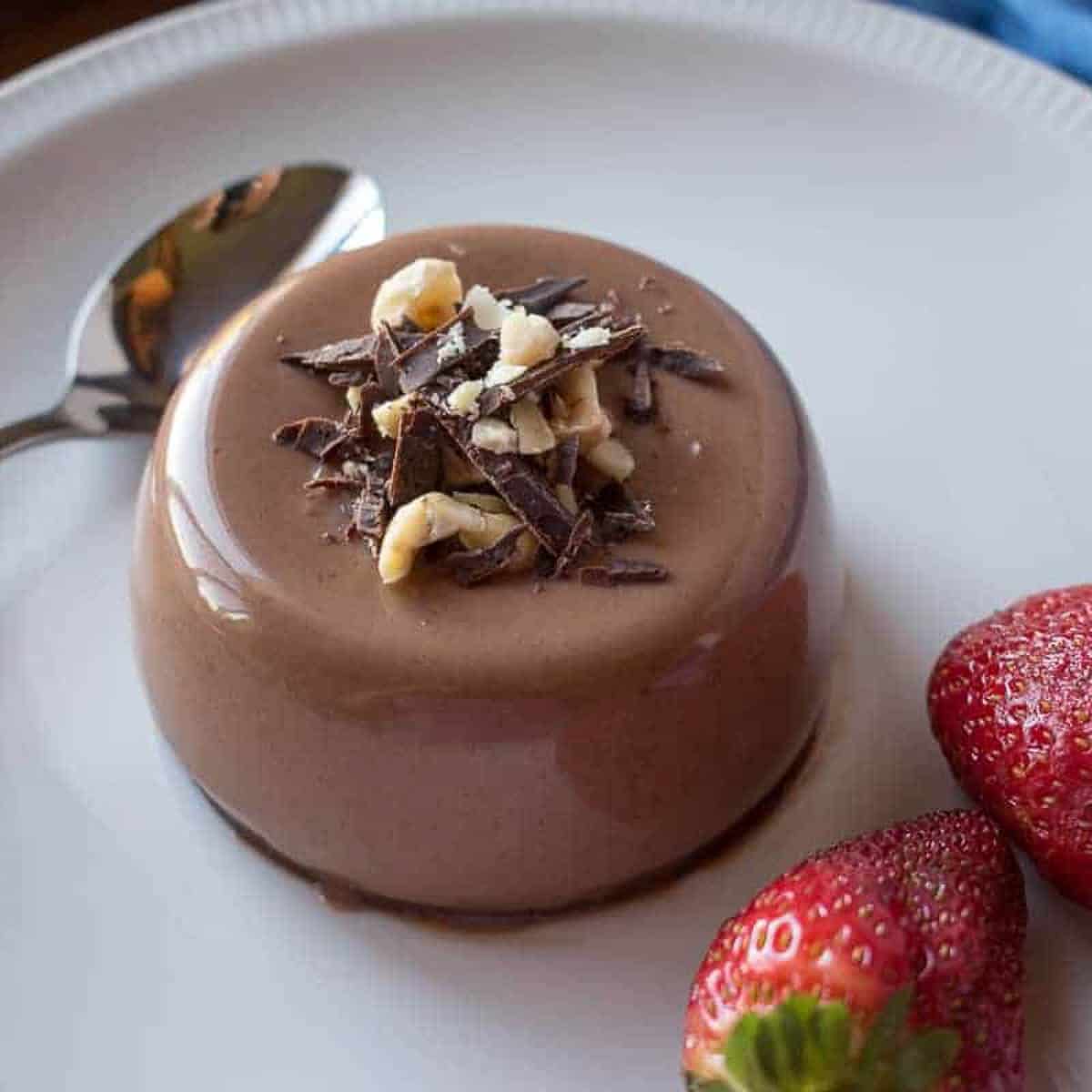 Chocolate panna cotta upturned on a white plate with strawberries on the side.