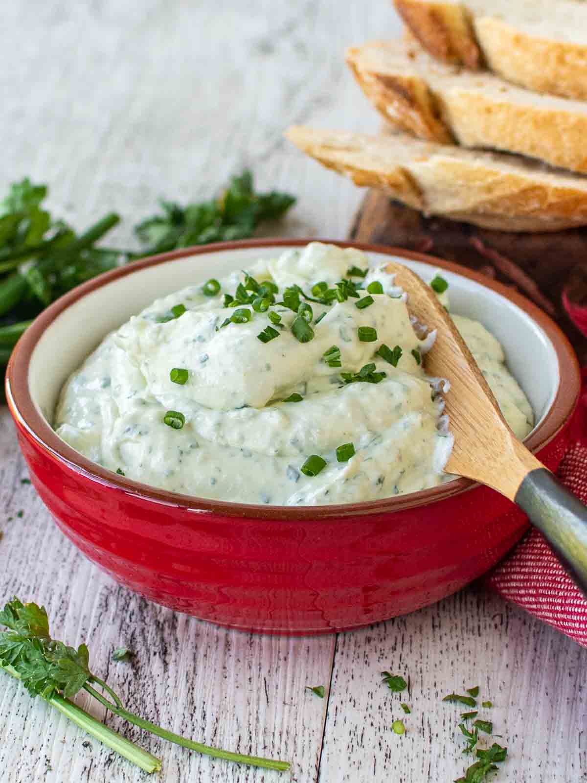 Garlic and herb cheese spread in a red bowl, garnished with chopped chives.