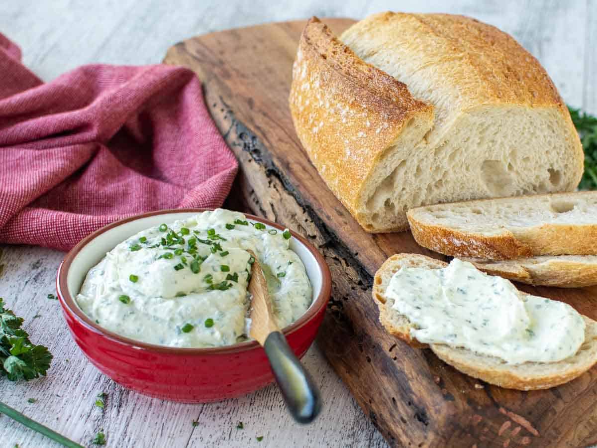 Creamy dip in a red bowl with loaf of partially sliced bread and creamy dip spread on one slice of bread.