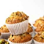 Two pistachio muffins stacked on a black wire rack with more muffins in the background.