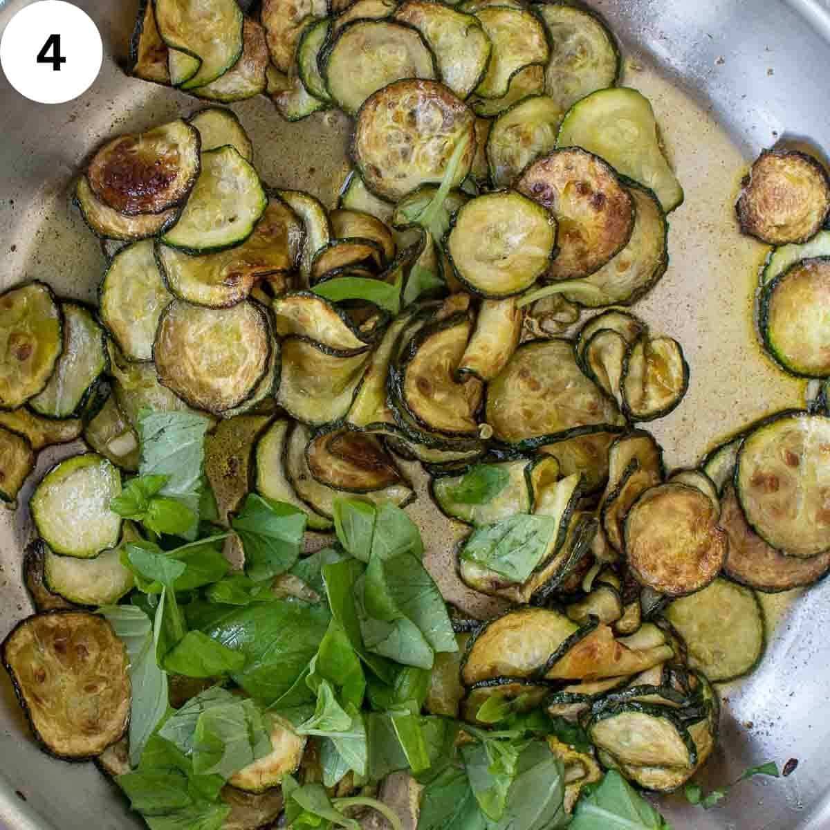 Fried zucchini rounds and torn basil leaves in a frying pan viewed from above.