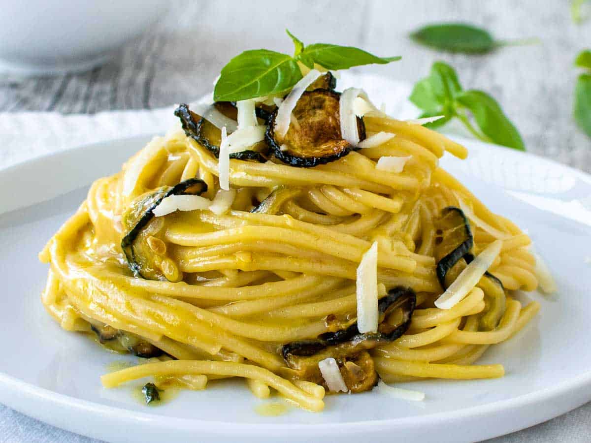 Close up of Spaghetti alla Nerano piled up on a white plate garnish with fried zucchini and extra cheese.