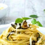 Spaghetti alla Nerano piled up on a white plate garnish with fried zucchini and extra cheese.