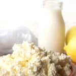Homemade Ricotta Cheese in a terracotta bowl with bottle of milk and a lemon in the background.