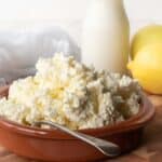 Homemade Ricotta Cheese in a terracotta bowl with bottle of milk and a lemon in the background.