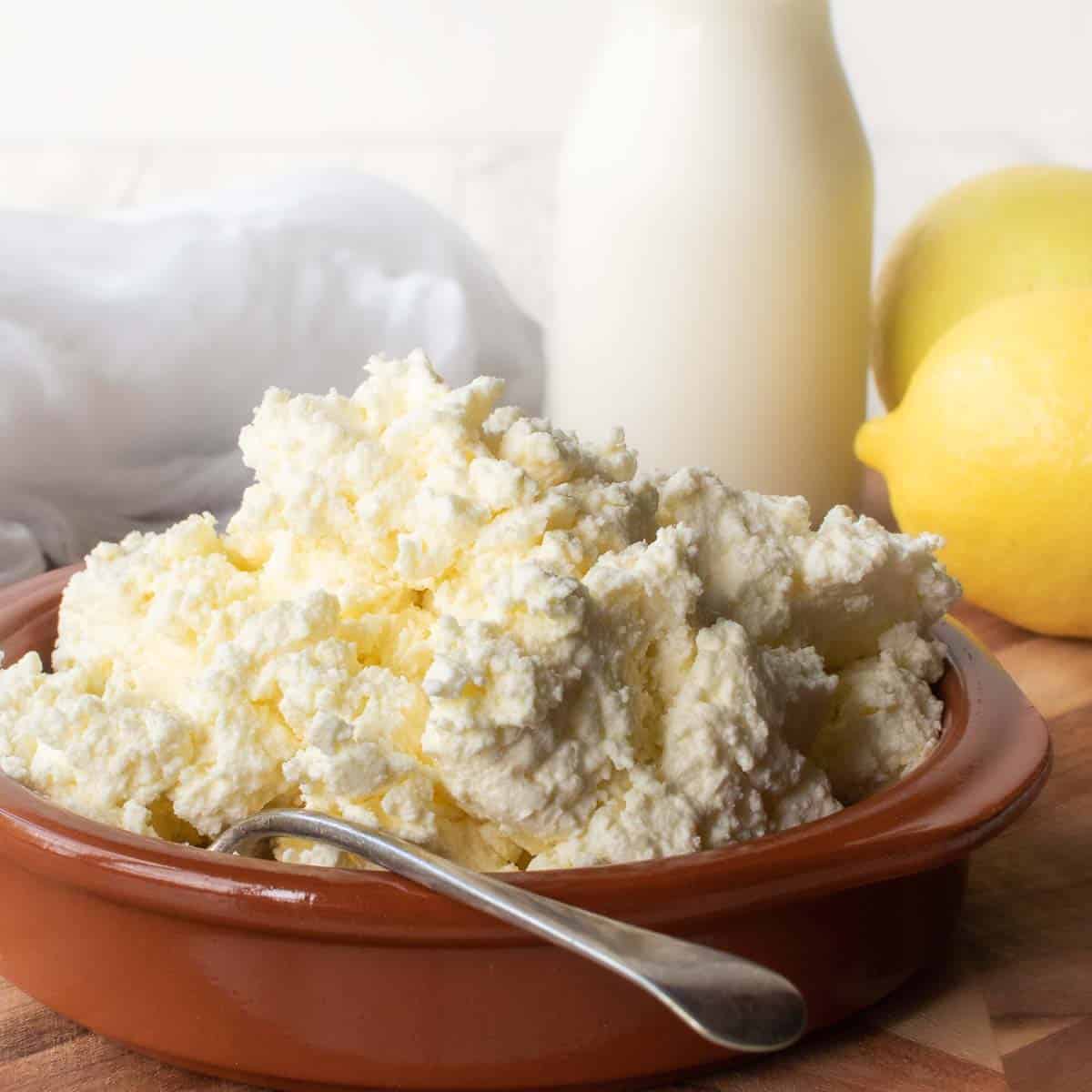 Homemade Ricotta Cheese in a terracotta bowl with bottle of milk and a lemon in the background.