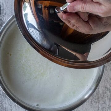Curdled milk in saucepan with lid being place on.