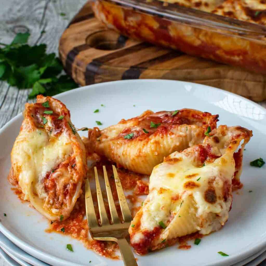Three giant cheese stuffed shells on a stack of white plates with a gold fork.