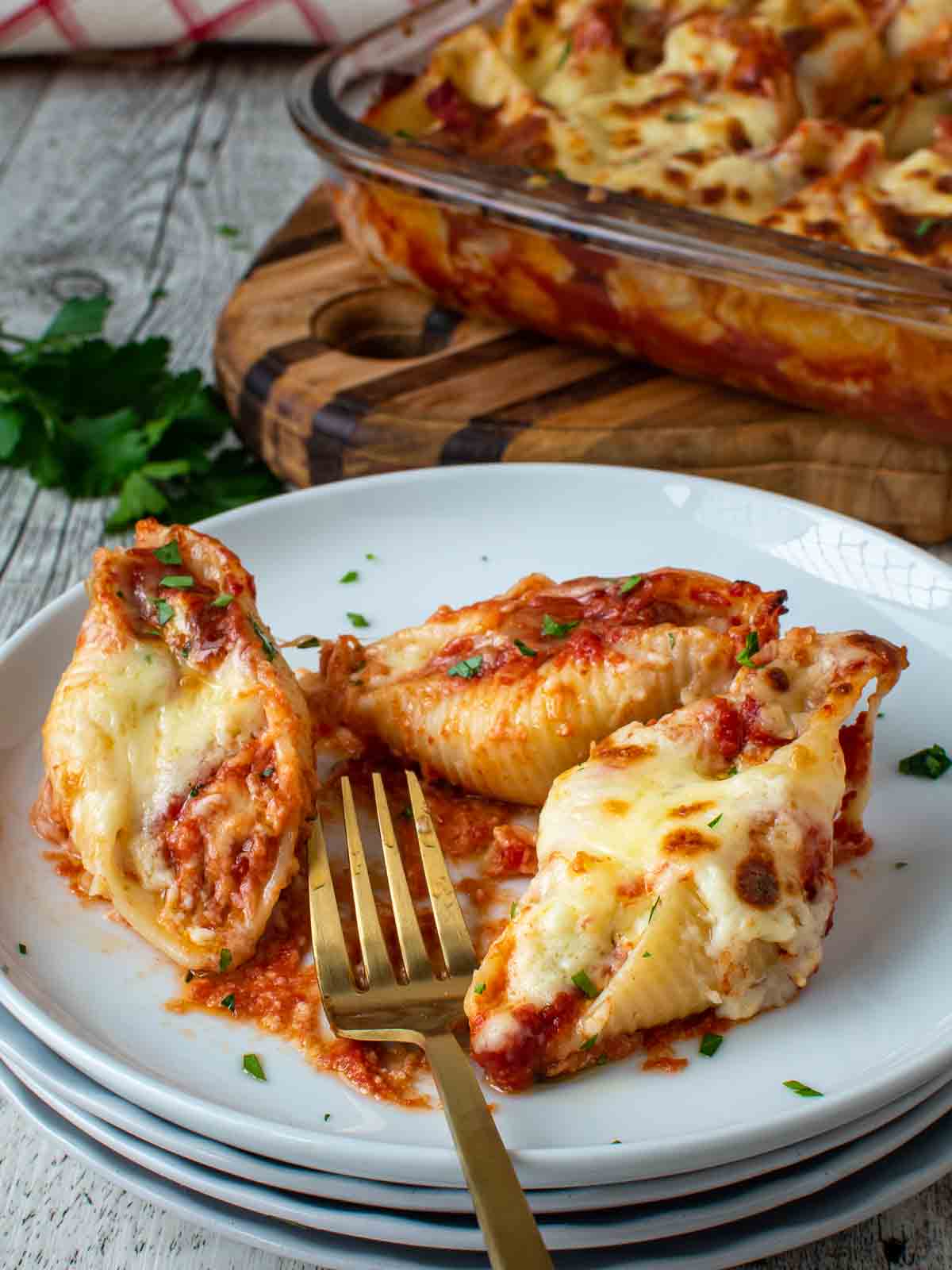 Three pasta shells stuffed with ricotta on a stack of white plates with a gold fork.