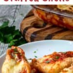 Three giant cheese stuffed shells on a stack of white plates with a gold fork.