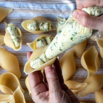 A clear piping bag filling large pasta shells with ricotta and parsley mixture.