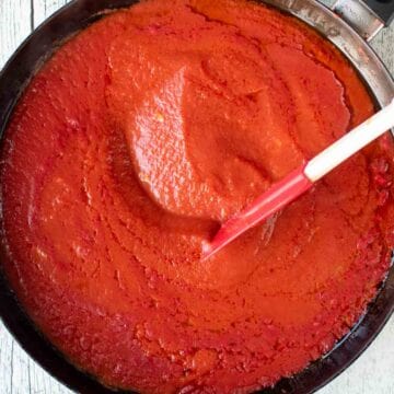 Tomato pasta sauce in a black skillet being stirred with a red spatula.