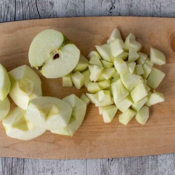 Peeled, halved, quartered and chopped apple on a wooden board.
